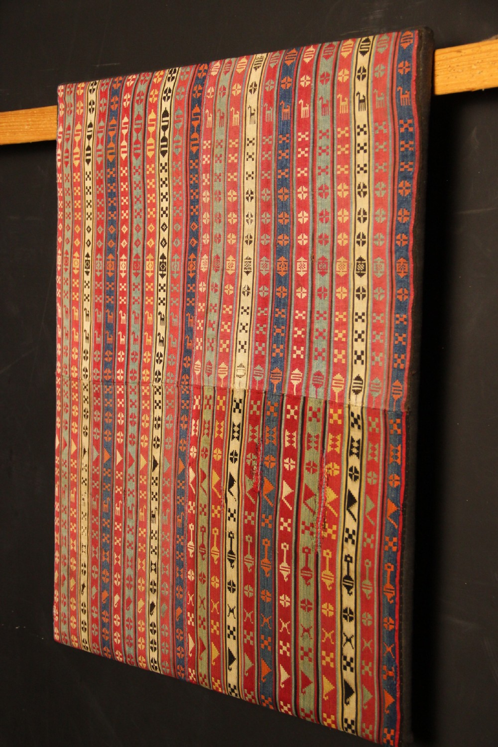 A rectangular mounted 19th-century silk jajim textile featuring vertical stripes with intricate geometric and stylized animal motifs in red, blue, cream, and yellow hues. View VII