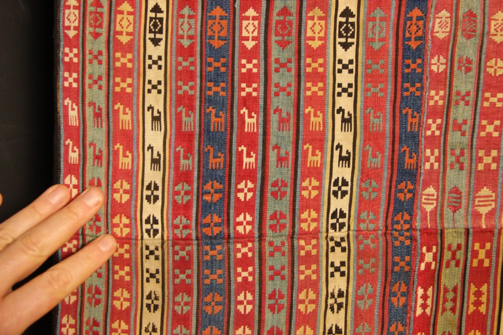 A rectangular mounted 19th-century silk jajim textile featuring vertical stripes with intricate geometric and stylized animal motifs in red, blue, cream, and yellow hues. View IX