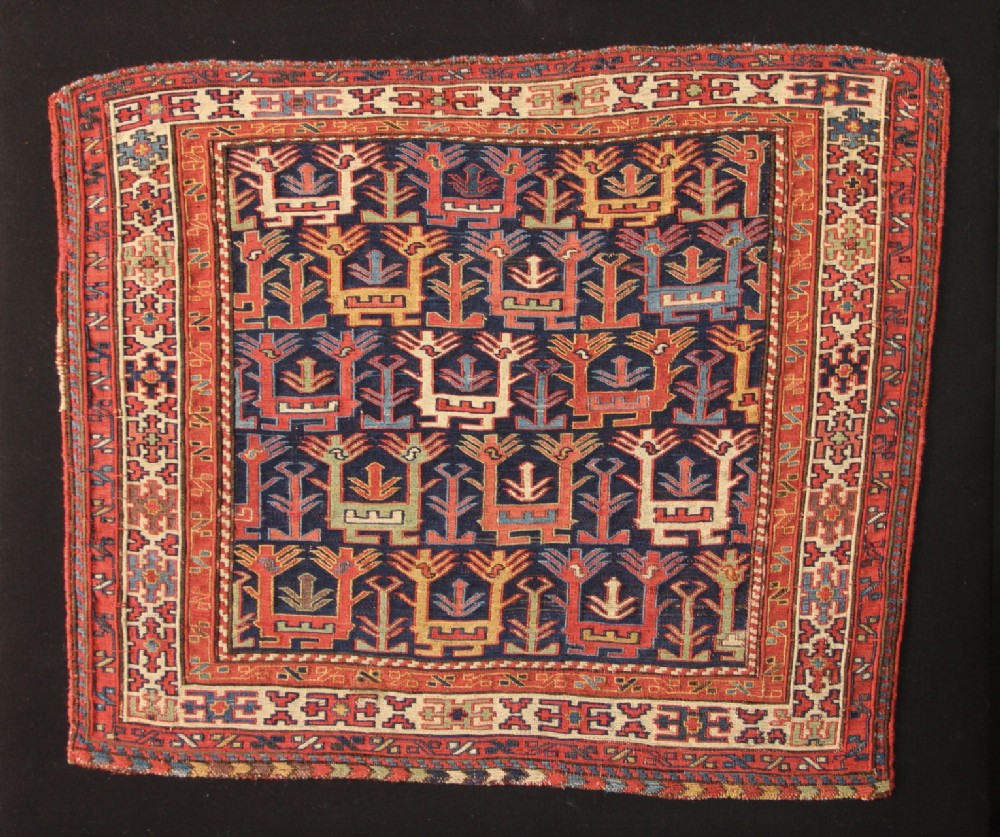 An antique Shahsavan soumak flat-weave wool textile featuring repeating stylised bird and plant motifs in red, blue, cream, and yellow on a dark blue field framed by geometric borders.