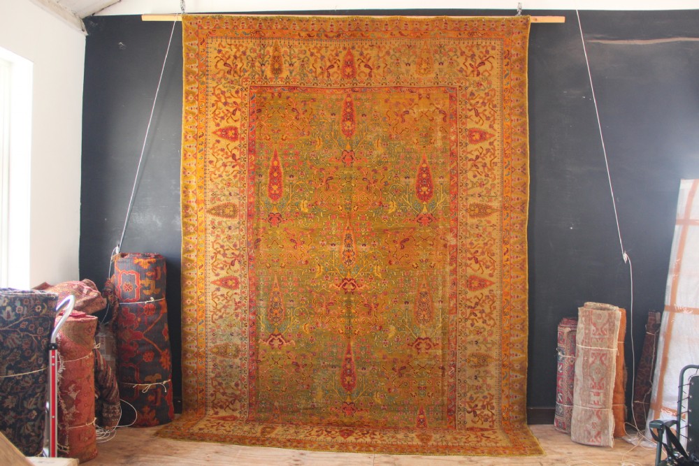 A large hand-knotted wool carpet featuring mustard yellow, olive green, and terracotta red tones with detailed floral and paisley motifs throughout.