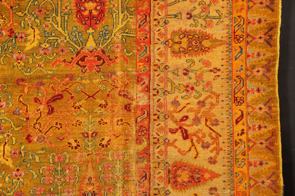 A large hand-knotted wool carpet featuring mustard yellow, olive green, and terracotta red tones with detailed floral and paisley motifs throughout. View IV