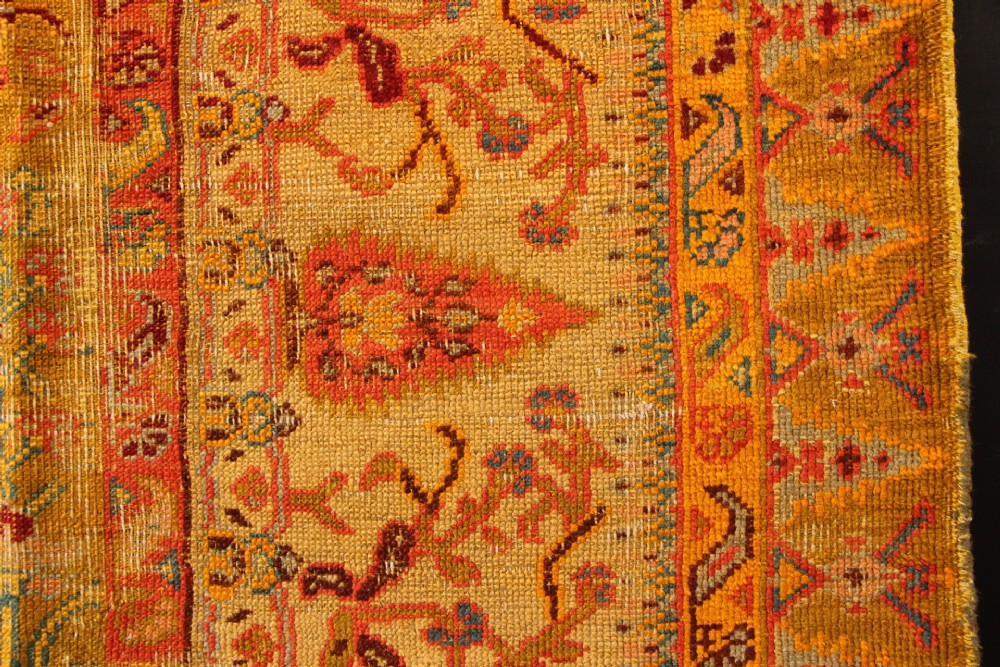 A large hand-knotted wool carpet featuring mustard yellow, olive green, and terracotta red tones with detailed floral and paisley motifs throughout. View V