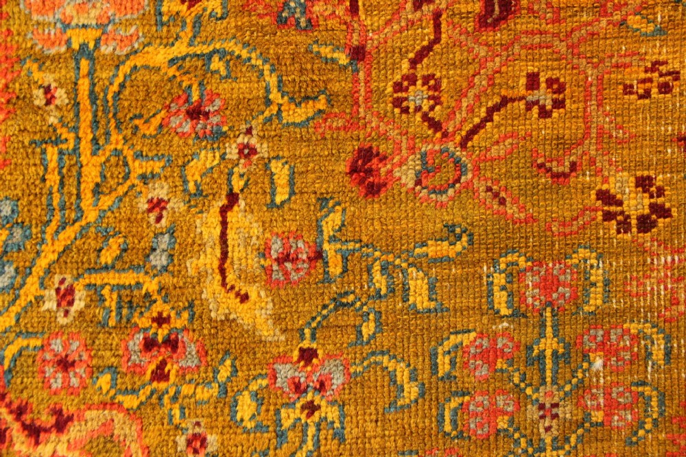 A large hand-knotted wool carpet featuring mustard yellow, olive green, and terracotta red tones with detailed floral and paisley motifs throughout. View VI