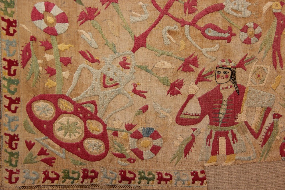 An antique hand-embroidered linen textile fragment from Skyros featuring red and green silk threads depicting human figures, birds, and floral motifs. View IV
