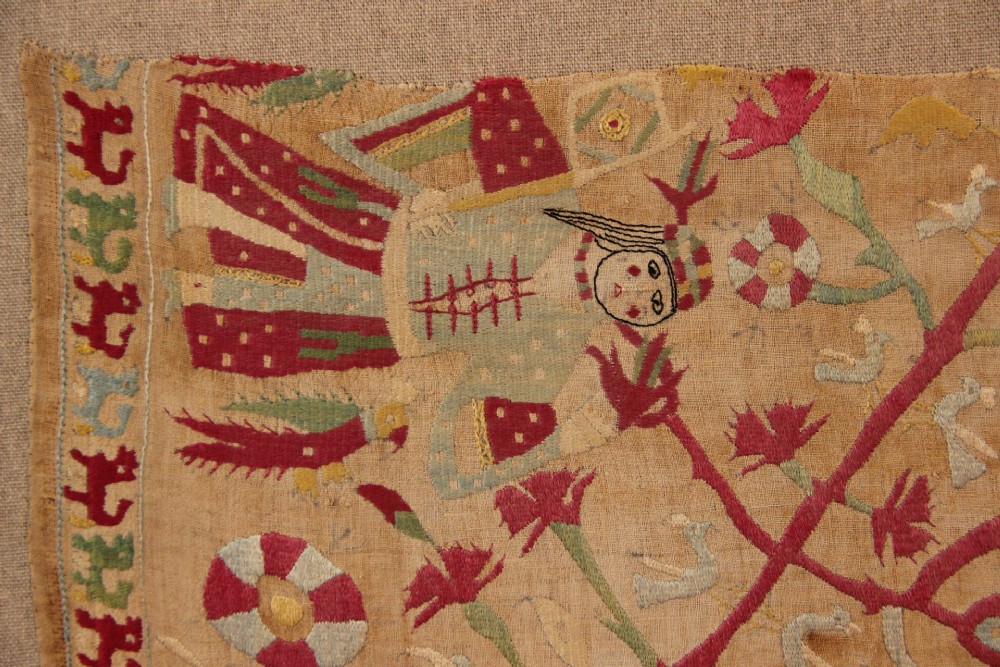 An antique hand-embroidered linen textile fragment from Skyros featuring red and green silk threads depicting human figures, birds, and floral motifs. View V