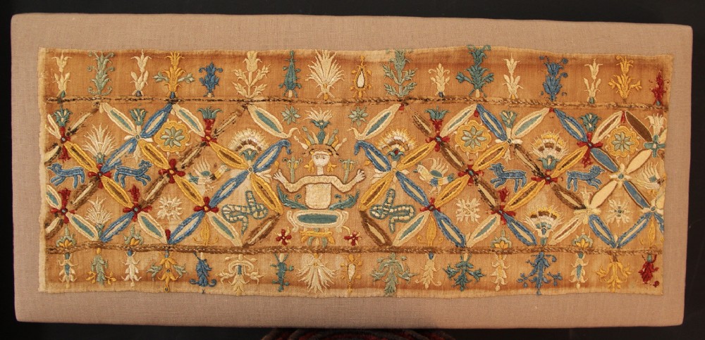 An 18th-century rectangular Cretan textile panel featuring polychrome silk embroidery on a natural beige linen ground with repeating geometric lattices, stylised human figures, birds, and floral motifs.