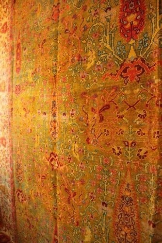 A large hand-knotted wool carpet featuring mustard yellow, olive green, and terracotta red tones with detailed floral and paisley motifs throughout. View VIII