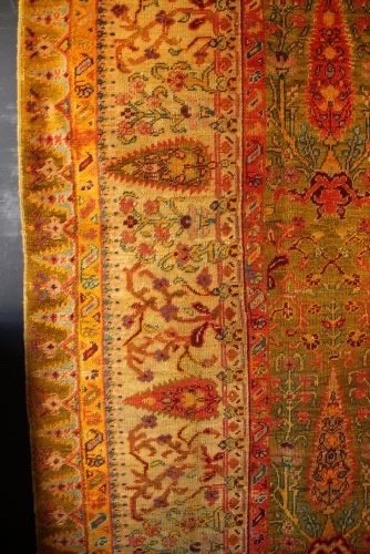 A large hand-knotted wool carpet featuring mustard yellow, olive green, and terracotta red tones with detailed floral and paisley motifs throughout. View IX
