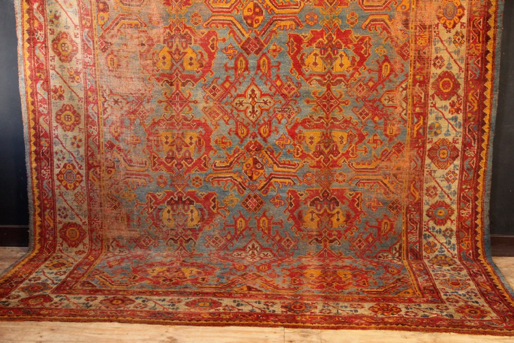 A large antique Turkish Oushak wool carpet featuring a pale blue field layered with terracotta and gold medallion motifs and a patterned border. View III