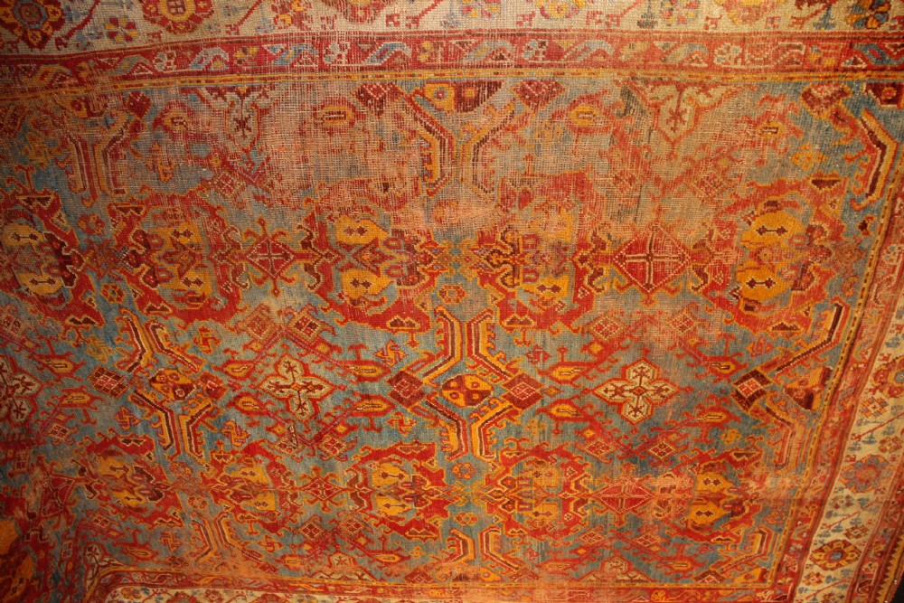 A large antique Turkish Oushak wool carpet featuring a pale blue field layered with terracotta and gold medallion motifs and a patterned border. View IV