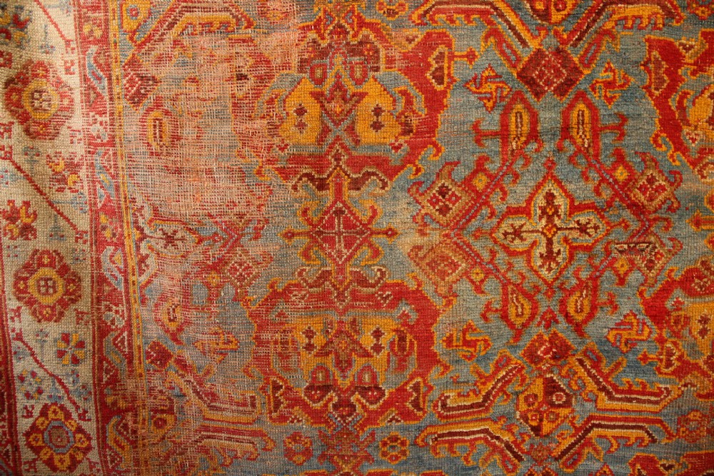 A large antique Turkish Oushak wool carpet featuring a pale blue field layered with terracotta and gold medallion motifs and a patterned border. View VI