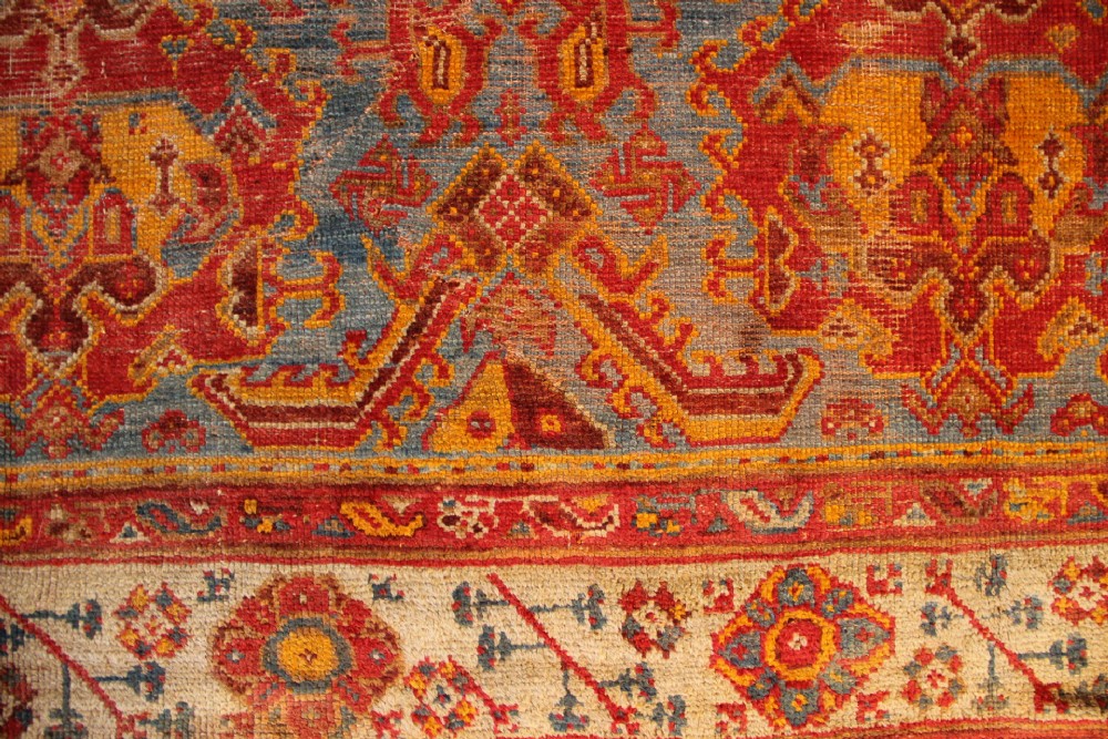 A large antique Turkish Oushak wool carpet featuring a pale blue field layered with terracotta and gold medallion motifs and a patterned border. View IX