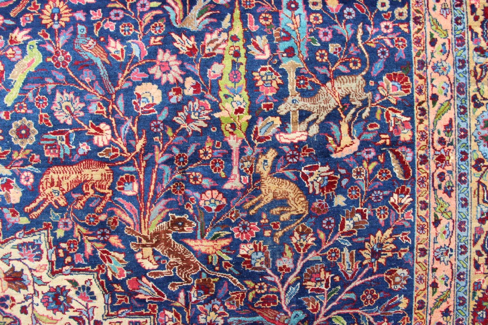 A large hand-knotted Persian Tabriz carpet featuring a central cream medallion surrounded by a navy blue field with intricate floral and hunting motifs, framed by a detailed red border. View VII