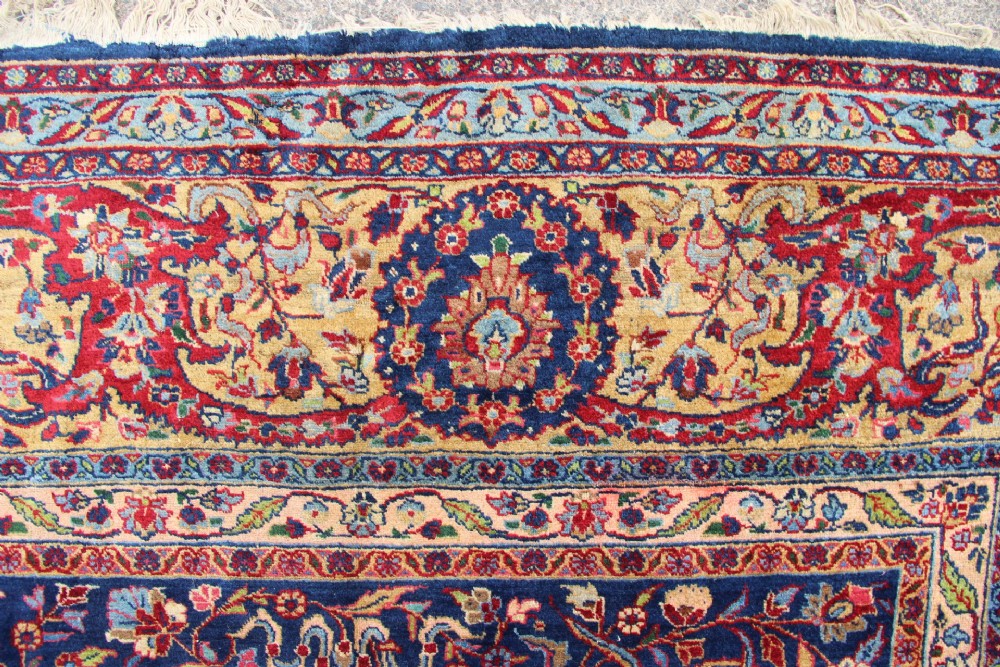 A large hand-knotted Persian Tabriz carpet featuring a central cream medallion surrounded by a navy blue field with intricate floral and hunting motifs, framed by a detailed red border. View XI