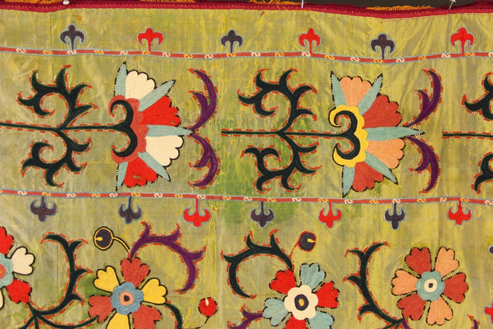 A rectangular green silk embroidered Suzani panel featuring a central circular solar motif flanked by intricate scrolling vines, botanical borders, and fringe edging. View XI