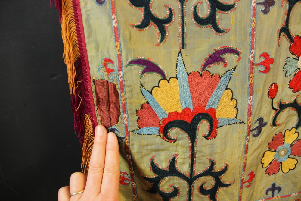 A rectangular green silk embroidered Suzani panel featuring a central circular solar motif flanked by intricate scrolling vines, botanical borders, and fringe edging. View XIII
