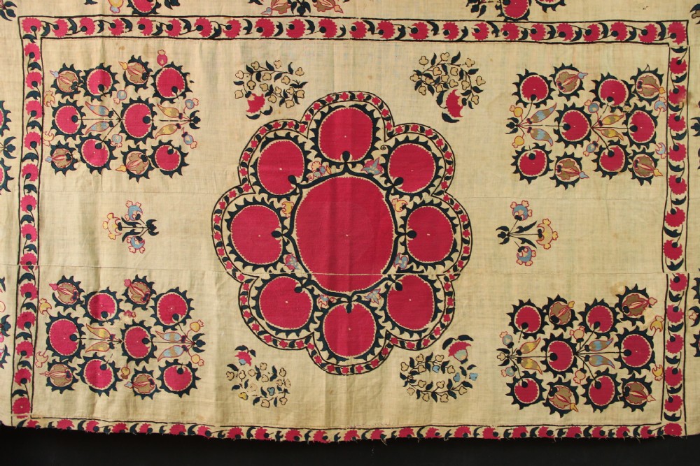 A rectangular hand-embroidered textile featuring central circular pomegranate motifs in crimson silk on a cream ground, framed by a floral border. View II