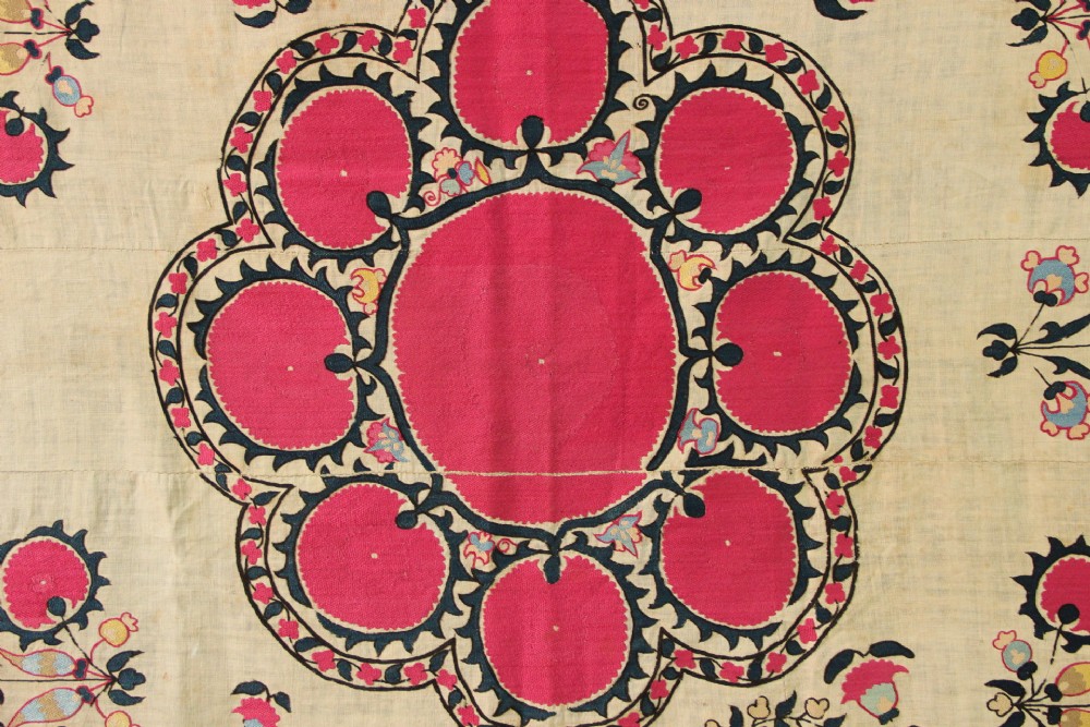 A rectangular hand-embroidered textile featuring central circular pomegranate motifs in crimson silk on a cream ground, framed by a floral border. View III