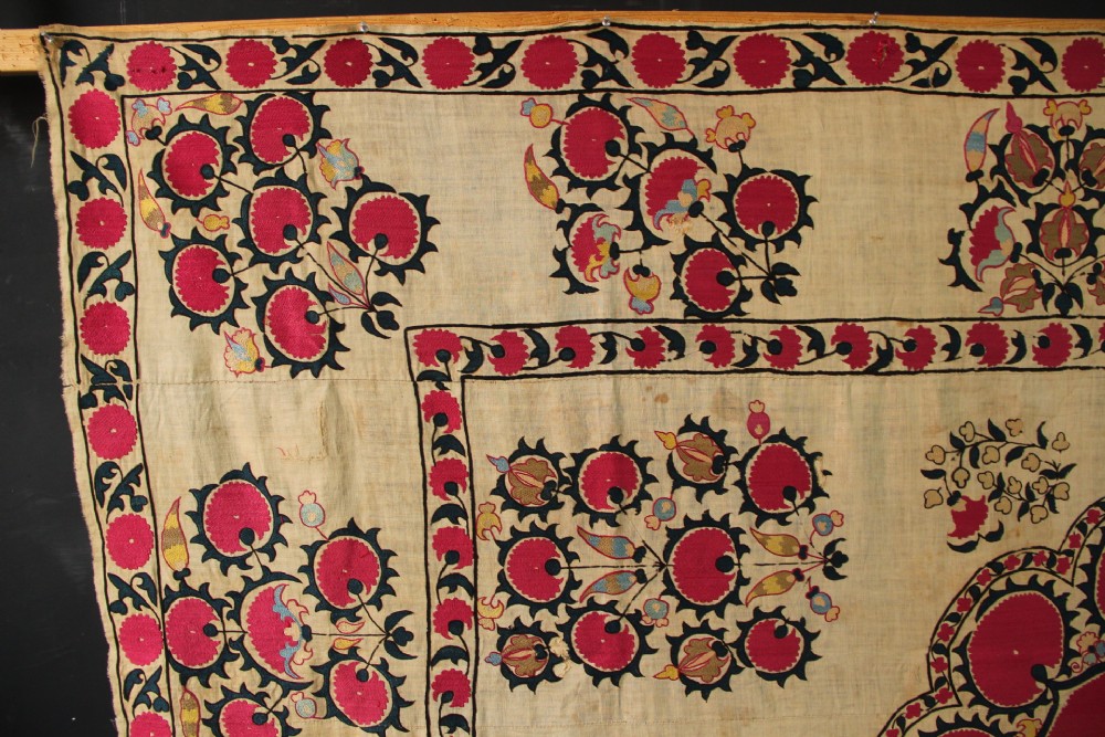 A rectangular hand-embroidered textile featuring central circular pomegranate motifs in crimson silk on a cream ground, framed by a floral border. View IV