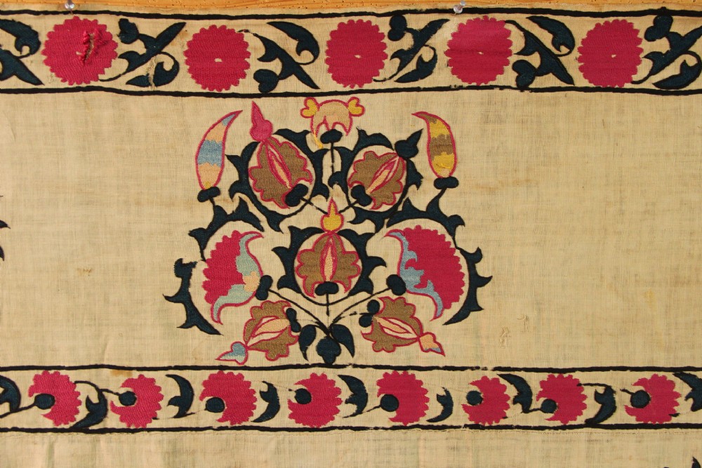 A rectangular hand-embroidered textile featuring central circular pomegranate motifs in crimson silk on a cream ground, framed by a floral border. View VI