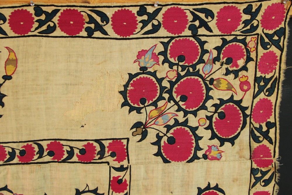 A rectangular hand-embroidered textile featuring central circular pomegranate motifs in crimson silk on a cream ground, framed by a floral border. View VII