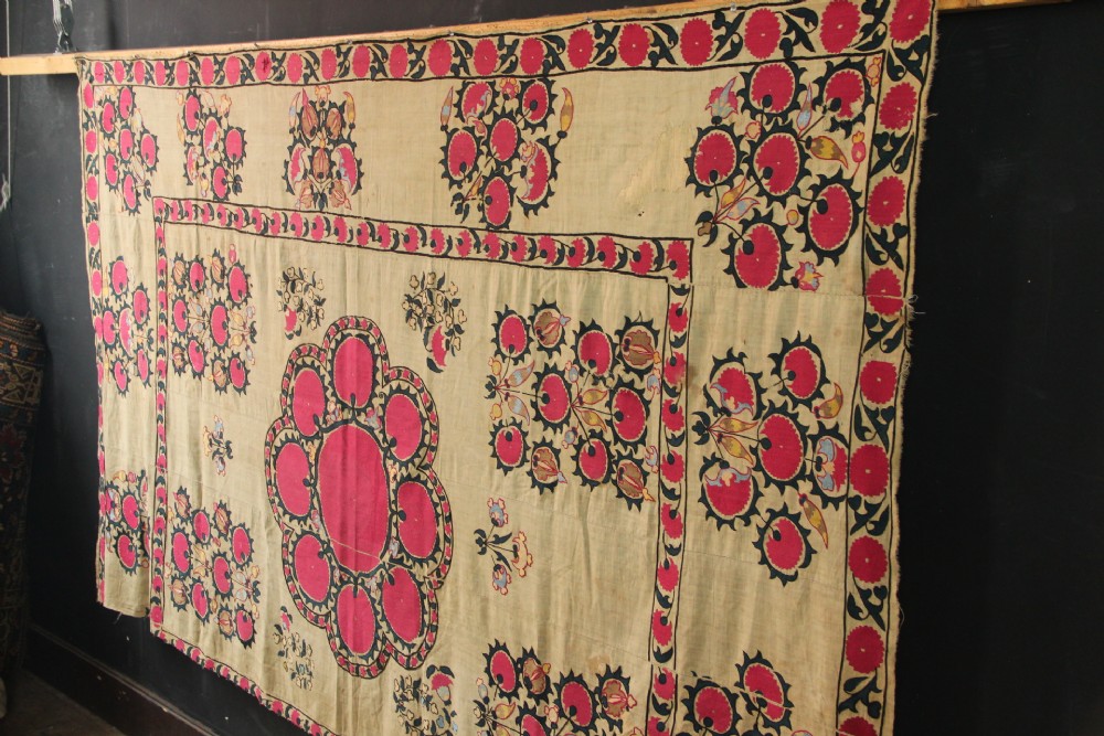 A rectangular hand-embroidered textile featuring central circular pomegranate motifs in crimson silk on a cream ground, framed by a floral border. View XII