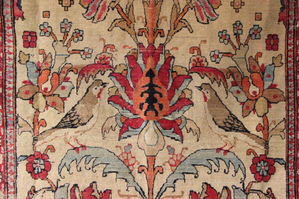 An antique hand-knotted Kirman Lavar wool rug featuring a central tree of life motif with birds and floral elements set on a cream field with a red border. View II