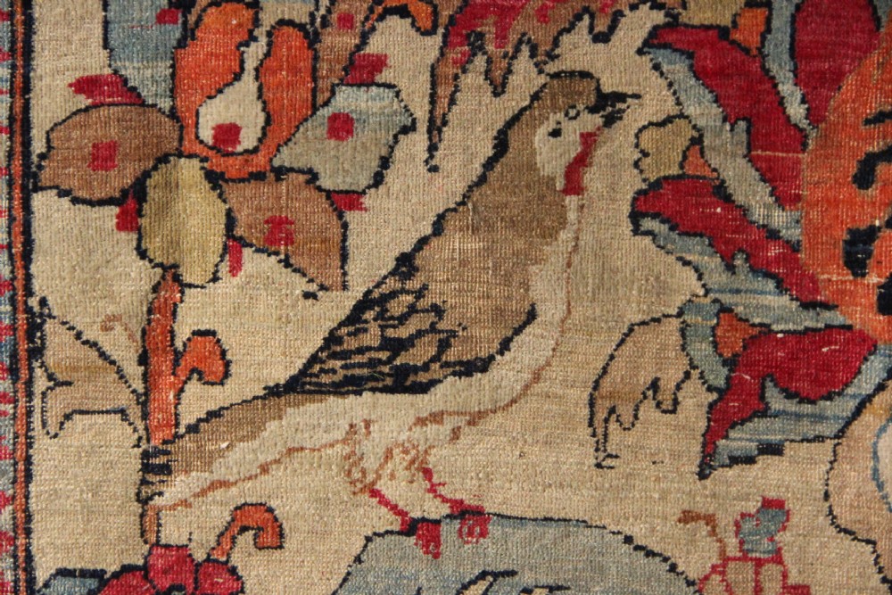 An antique hand-knotted Kirman Lavar wool rug featuring a central tree of life motif with birds and floral elements set on a cream field with a red border. View III