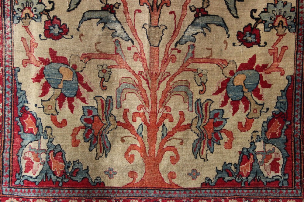 An antique hand-knotted Kirman Lavar wool rug featuring a central tree of life motif with birds and floral elements set on a cream field with a red border. View V