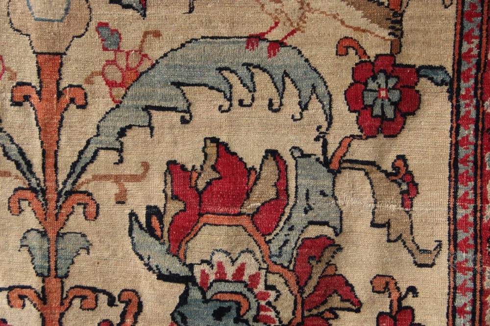 An antique hand-knotted Kirman Lavar wool rug featuring a central tree of life motif with birds and floral elements set on a cream field with a red border. View VI