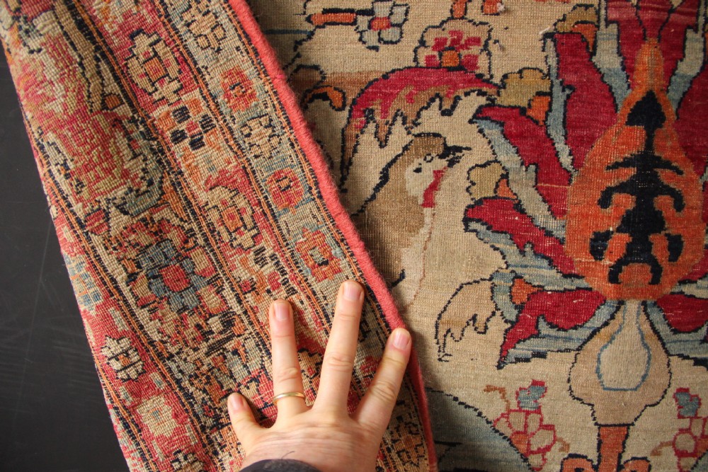 An antique hand-knotted Kirman Lavar wool rug featuring a central tree of life motif with birds and floral elements set on a cream field with a red border. View IX