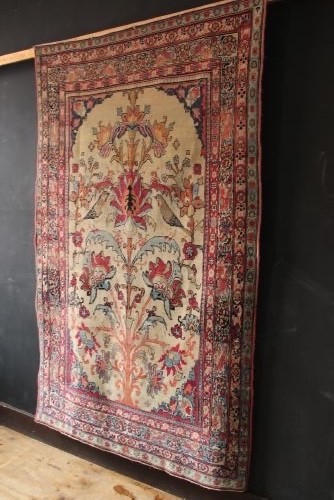An antique hand-knotted Kirman Lavar wool rug featuring a central tree of life motif with birds and floral elements set on a cream field with a red border. View VIII