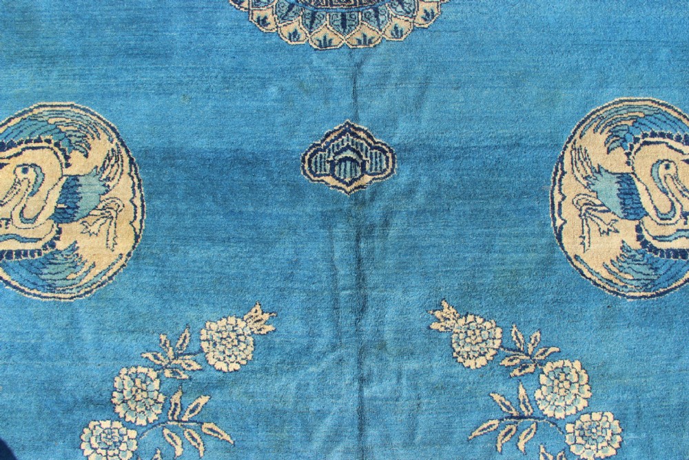 A large rectangular antique Chinese wool carpet featuring a vibrant blue field decorated with circular roundels and floral motifs, enclosed by a wide beige decorative border. View III