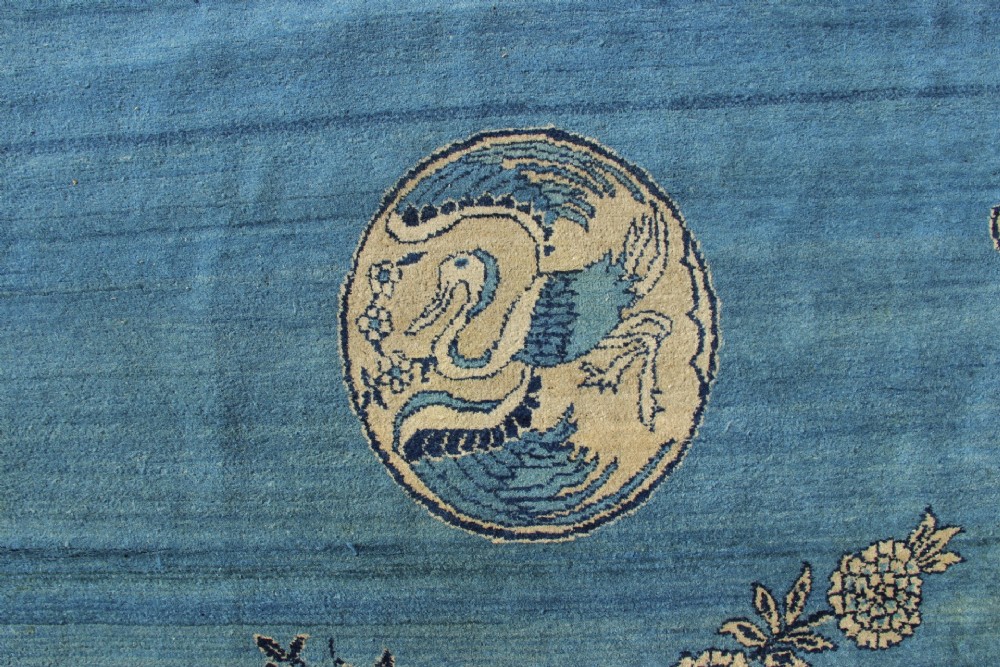 A large rectangular antique Chinese wool carpet featuring a vibrant blue field decorated with circular roundels and floral motifs, enclosed by a wide beige decorative border. View IV