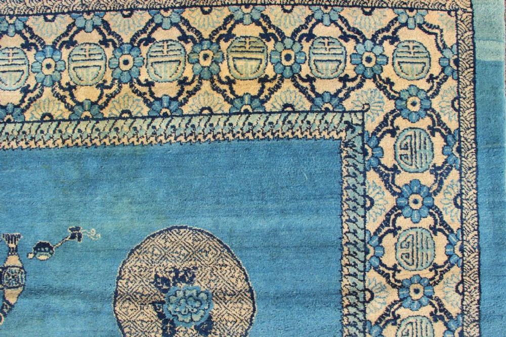 A large rectangular antique Chinese wool carpet featuring a vibrant blue field decorated with circular roundels and floral motifs, enclosed by a wide beige decorative border. View V