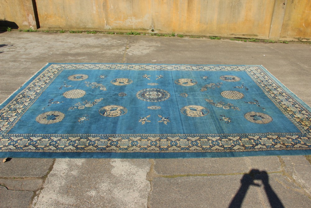 A large rectangular antique Chinese wool carpet featuring a vibrant blue field decorated with circular roundels and floral motifs, enclosed by a wide beige decorative border. View VII