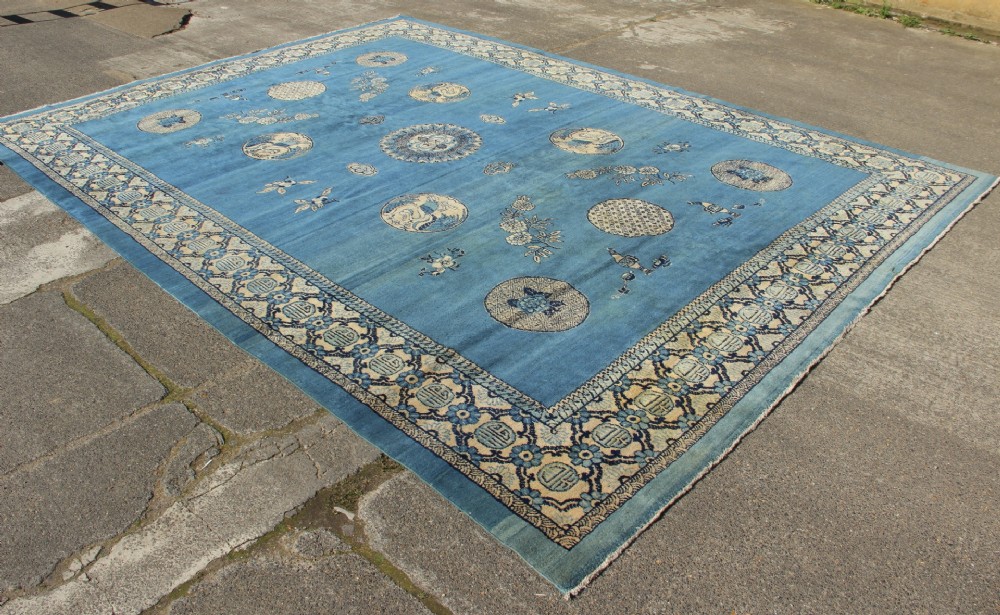 A large rectangular antique Chinese wool carpet featuring a vibrant blue field decorated with circular roundels and floral motifs, enclosed by a wide beige decorative border. View VIII