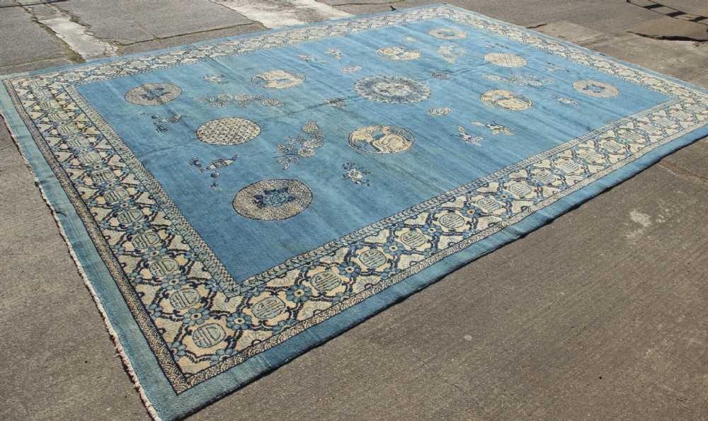 A large rectangular antique Chinese wool carpet featuring a vibrant blue field decorated with circular roundels and floral motifs, enclosed by a wide beige decorative border. View X