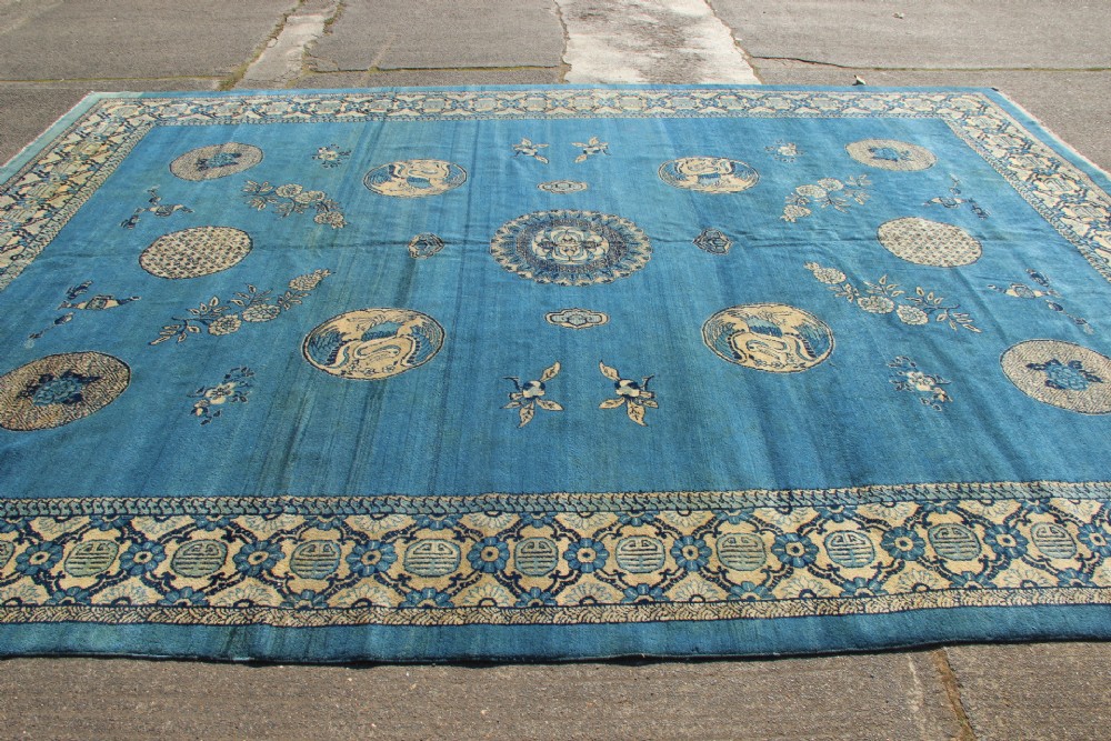 A large rectangular antique Chinese wool carpet featuring a vibrant blue field decorated with circular roundels and floral motifs, enclosed by a wide beige decorative border. View XI
