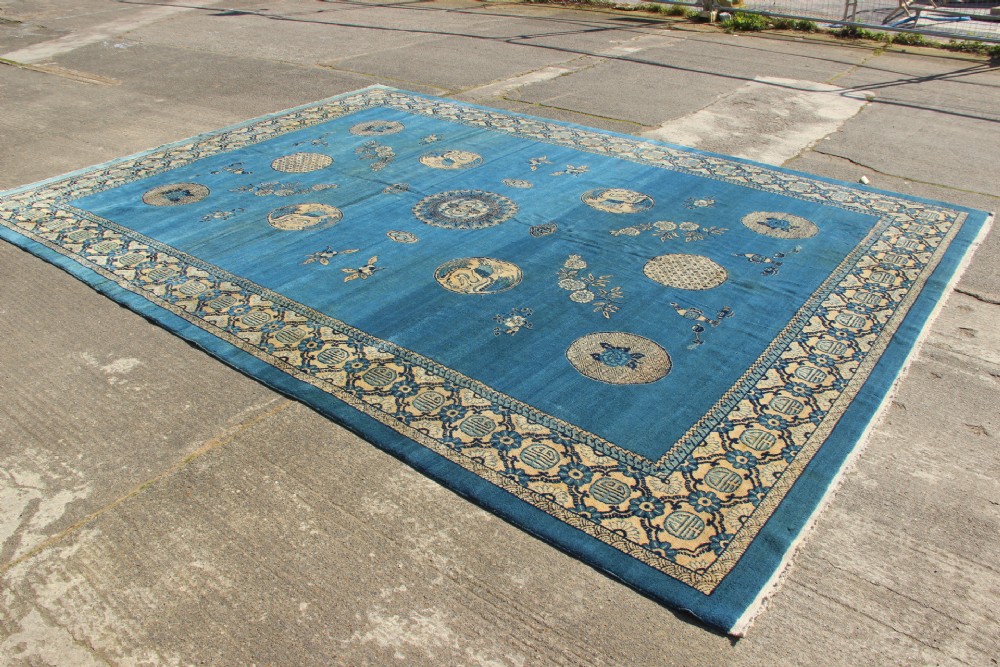 A large rectangular antique Chinese wool carpet featuring a vibrant blue field decorated with circular roundels and floral motifs, enclosed by a wide beige decorative border. View XII