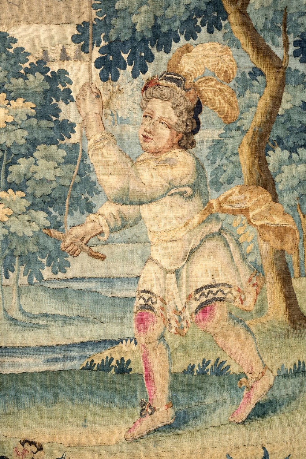 An 18th-century Audenaarde woven tapestry depicting two figures in a wooded landscape with a floral border. View II