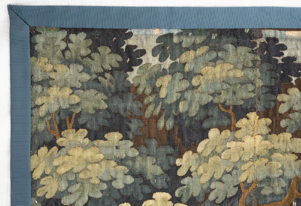 An 18th-century Audenaarde woven tapestry depicting two figures in a wooded landscape with a floral border. View IV