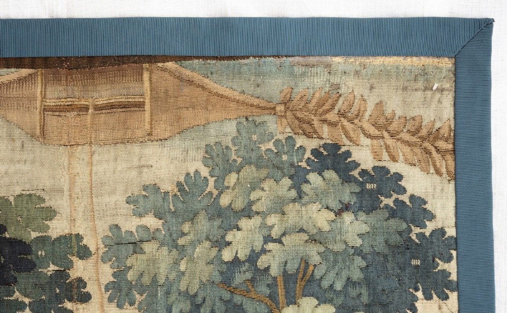 An 18th-century Audenaarde woven tapestry depicting two figures in a wooded landscape with a floral border. View VI