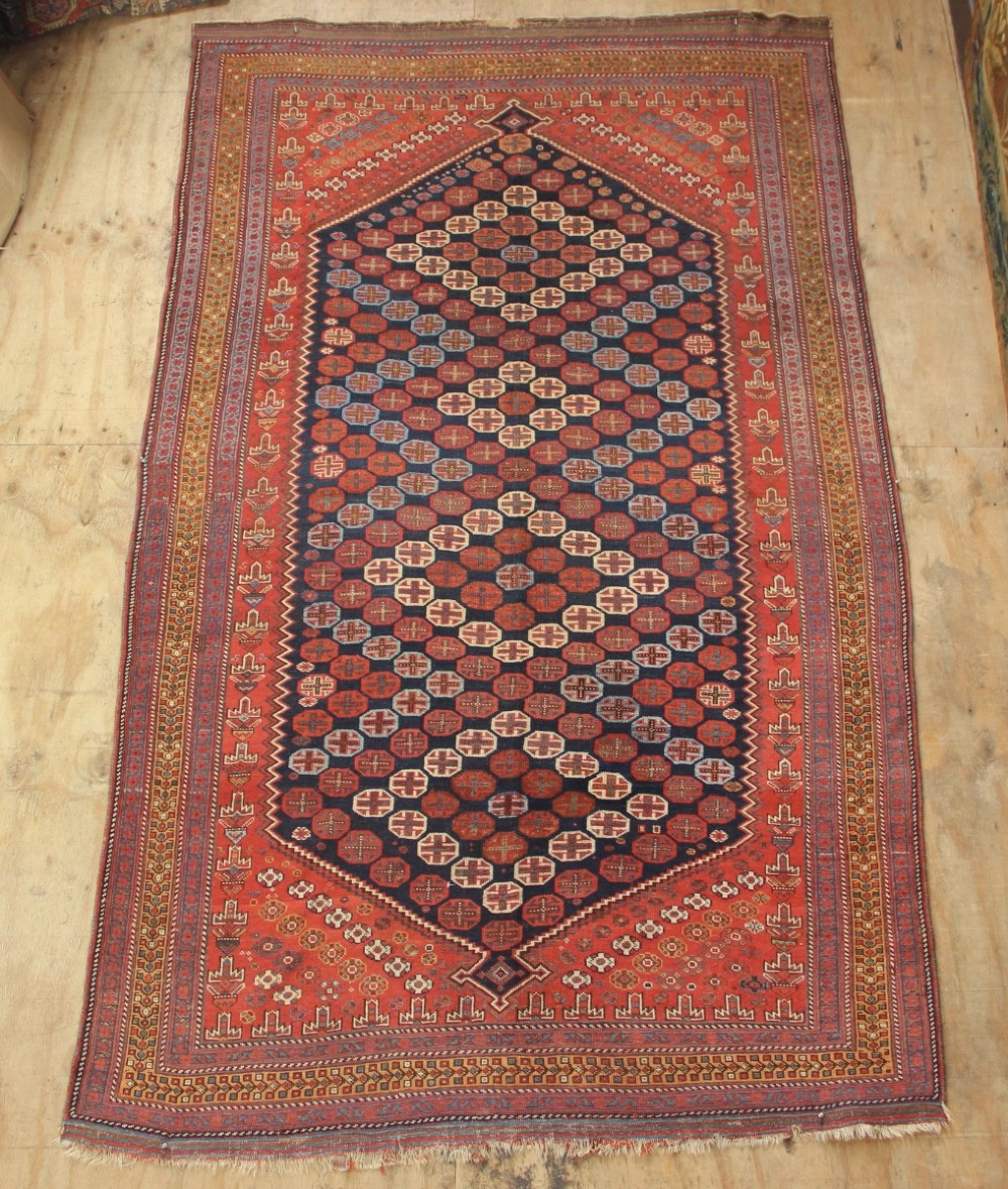 A hand-knotted rectangular wool carpet featuring a dark navy blue hexagonal field adorned with repeating geometric lattice motifs, surrounded by a bold terracotta red border.