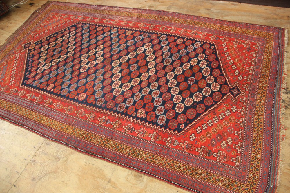 A hand-knotted rectangular wool carpet featuring a dark navy blue hexagonal field adorned with repeating geometric lattice motifs, surrounded by a bold terracotta red border. View III