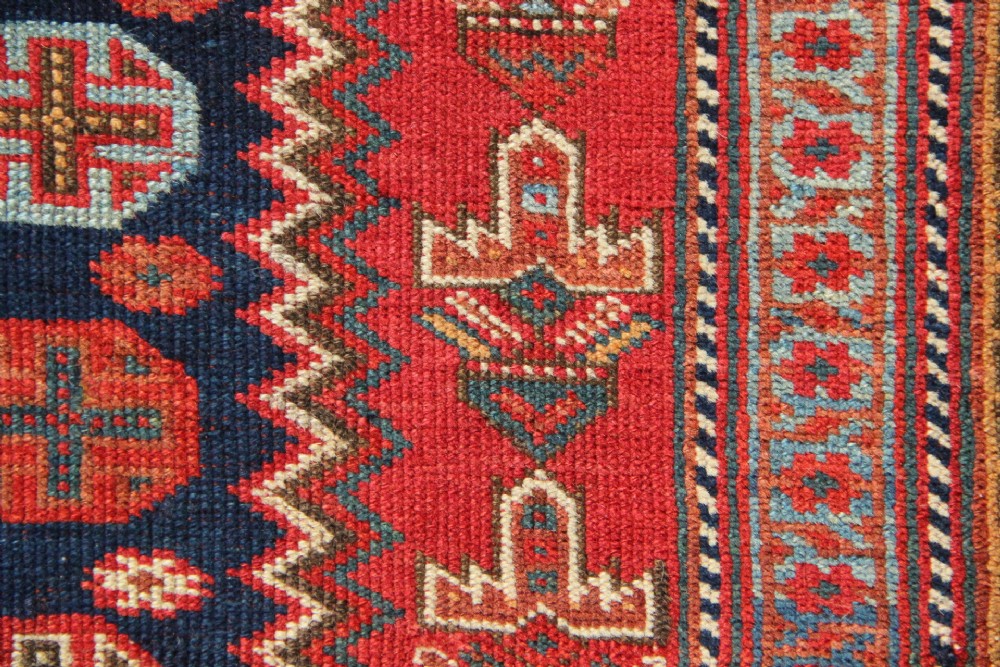 A hand-knotted rectangular wool carpet featuring a dark navy blue hexagonal field adorned with repeating geometric lattice motifs, surrounded by a bold terracotta red border. View VIII