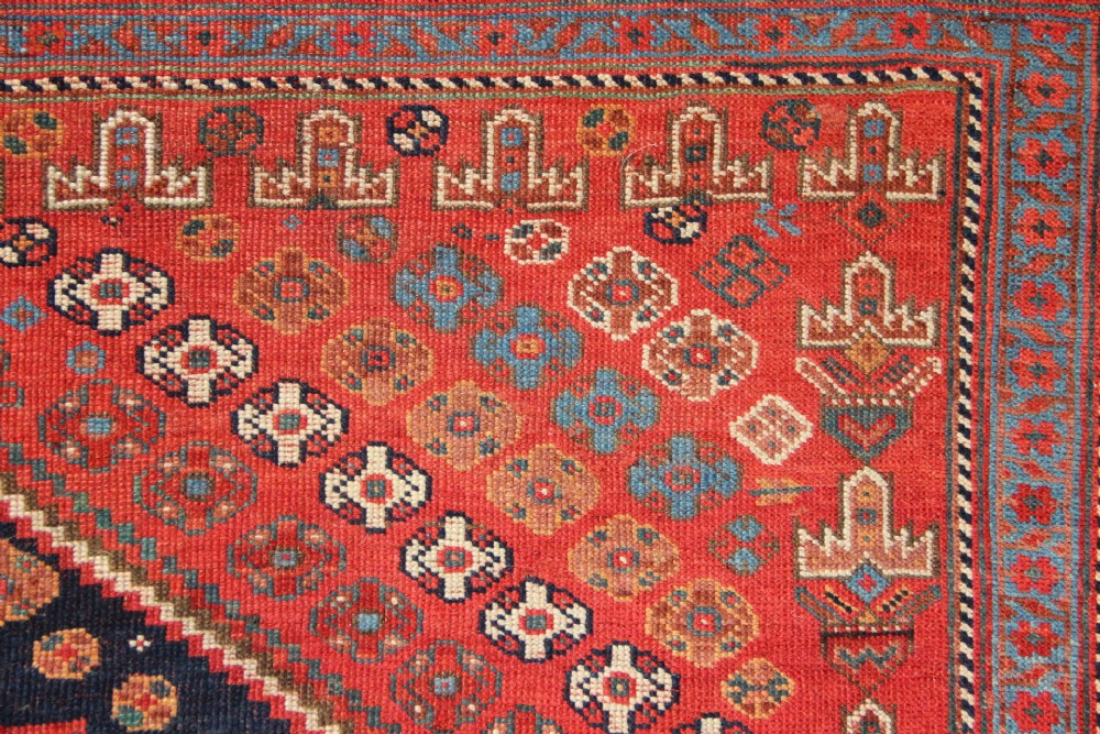 A hand-knotted rectangular wool carpet featuring a dark navy blue hexagonal field adorned with repeating geometric lattice motifs, surrounded by a bold terracotta red border. View IX