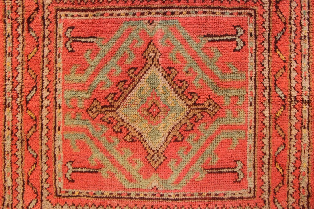 A square hand-knotted antique Oushak wool mat featuring a central geometric diamond medallion in coral red, sage green, and taupe tones. View II