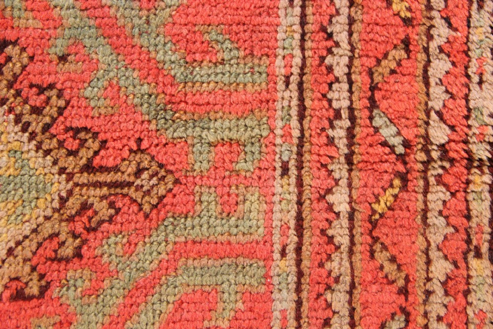 A square hand-knotted antique Oushak wool mat featuring a central geometric diamond medallion in coral red, sage green, and taupe tones. View III