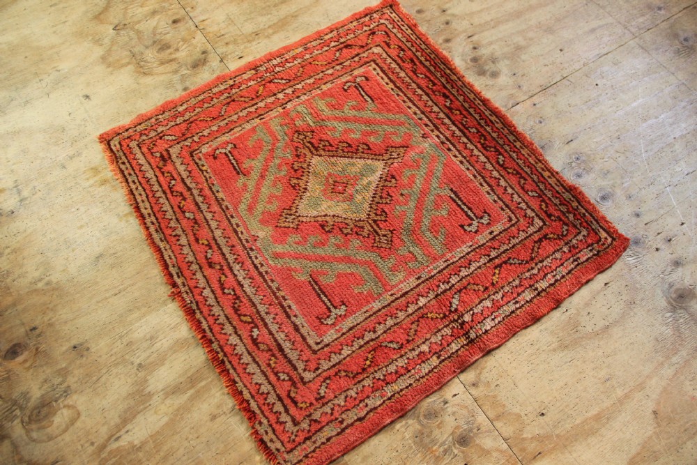 A square hand-knotted antique Oushak wool mat featuring a central geometric diamond medallion in coral red, sage green, and taupe tones. View IV